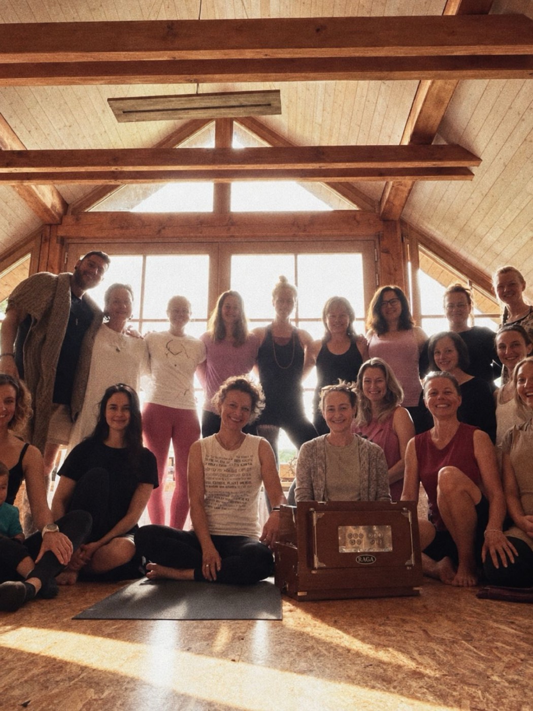Skupinová fotografie účastníků Jivamukti Yoga Retreatu s harmoniem ve dřevěné světnici
